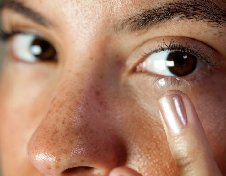 Woman putting on contact lens in her left eye