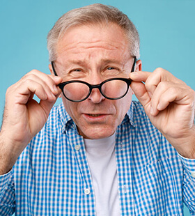 Man with cataracts pulling down glasses squinting